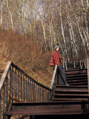 A woman in a gray skirt and pantyhose, wearing a green hat and a red jacket, is sitting on the railing of long staircase.