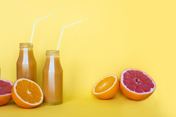Fresh orange juice in bottles with oranges on yellow background. Place for your text