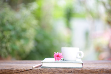 White coffee cup and notebook with pink pygmy rose on wooden table