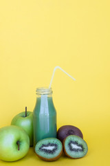 Green smoothie in bottle and ingredients on yellow background with copy space