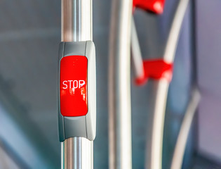 Red stop button on the metal handrail of a bus