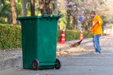 Green trash bin with asian man worker cleaning the road background.