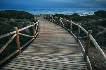 Lumber pathway leading to rippling sea on tranquil evening in countryside in Cabopino, Artola dunes. Marbella, Spain