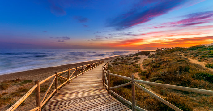 View of amazing bright sundown sky over waving sea and wooden path in countryside in Cabopino, Artola dunes. Marbella, Spain