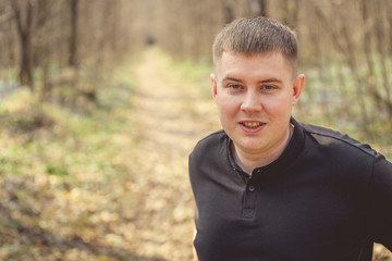 A young male among the trees. Portrait of a young attractive man standing  in autumnal park covered with foliage in daytime