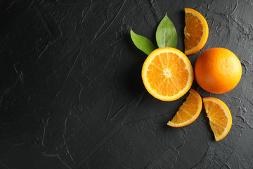 Oranges with pieces and leaves on black background. Space for text, top view