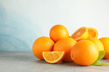 Ripe oranges with leaves on grey table against light background, space for text