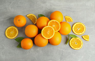 Many ripe oranges and leaves with space for text on grey table, top view