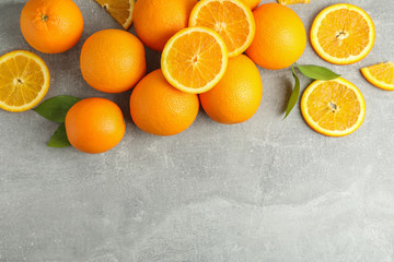Many ripe oranges and leaves with space for text on grey table, top view