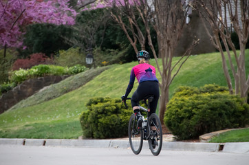 Woman riding bike in spring neighborhood with spandex riding gear and helmet down street with pink...