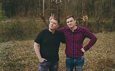 Young smiling friends in modern clothes. Two men posing in the woods.  The concept of male friendship