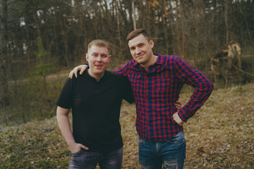 Young smiling friends in modern clothes. Two men posing in the woods.  The concept of male friendship