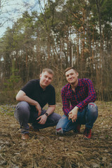 Men sitting on ground in spring day Young smiling friends in modern clothes sitting on ground with old foliage and looking at camera