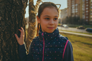 Girl near tree in park. Girl while standing near tree trunk on sunny and windy day in city park