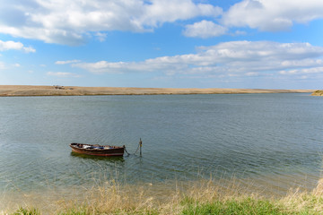 Obraz premium An empty rowing boat moored by the edge of the water. Taken on the Fleet lagoon in Dorset, United Kingdom. Chesil beach is visible in the distance.