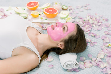 Obraz na płótnie Canvas Young healthy woman in spa making treatments and face mask, natural cosmetics and fruits around her. Young woman in a spa with algae facial mask.