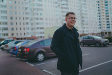 Man standing in yard of city Portrait of young man in casual clothes standing beside cars in yard of high-rise buildings