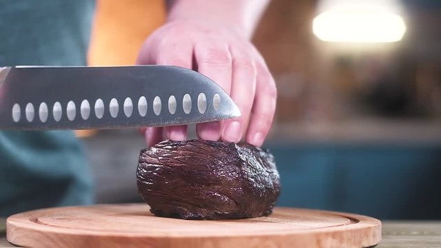 chef cuts beef into pieces with a sharp knife. Slow motion.