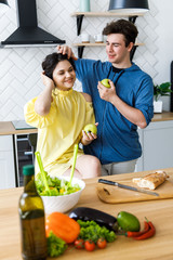 Young cute smiling couple cooking together at kitchen at home. A couple - a girl and a boy who spend time together for cooking. The guy and girl eat green apples