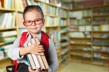 Cute little schoolgirl in glasses on library background