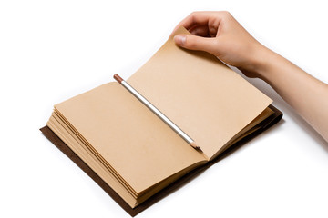 female hand turns over a page of an open craft notepad on which lies a gray pencil on a white background