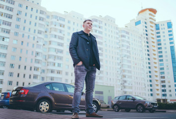Man standing in yard of city Portrait of young man in casual clothes standing beside cars in yard of high-rise buildings
