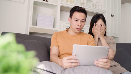 Fototapeta premium Asian couple using tablet for online shopping in internet in living room at home, sweet couple enjoy love moment while lying on the sofa when relax at home. Lifestyle couple relax at home concept.