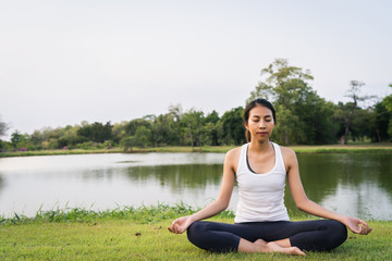 Naklejka na ściany i meble Young asian woman yoga outdoors keep calm and meditates while practicing yoga to explore the inner peace. Yoga have good benefits for health near lake at park. Sport and Healthy lifestyle concept.