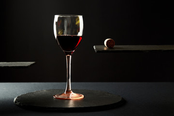 Composition of red wine in glass and corck on black background.