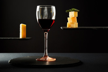 Portion of red wine and pieces of cheese on black background