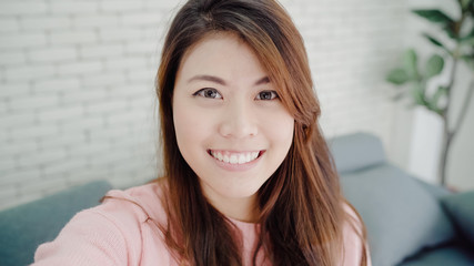 Asian blogger woman using smartphone recording vlog video in living room at home,female enjoy funny...
