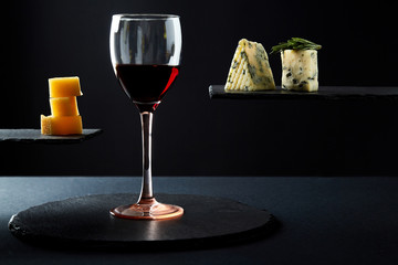 Red wine in glass and pieces of different sorts of aromatic cheese