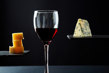 Red wine in glass and pieces of different sorts of aromatic cheese