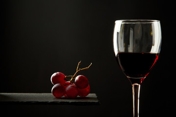 Composition of red wine in glass beside blue cheese and grape on black background.