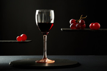 Sweet red wine in glass and fresh grape berries on black background