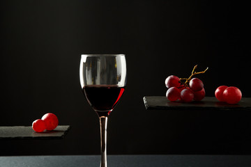 Sweet red wine in glass and fresh grape berries on black background