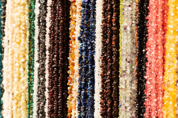 Colorful strings of stone beads hang from a vendors display and sparkle in the sun.