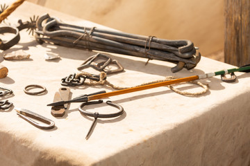 Various metal objects made by a traditional blacksmith such as buckles, tent pegs and a handmade arrow are displayed on a table.
