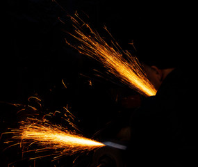 Fire sparks on a black background during workers sharpen a knife.