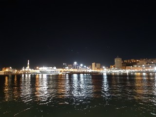 Genova, Italy - 04/19/2019: An amazing caption of the sea shore of Genoa by night in spring with some beautiful lights of the sheeps and a great view to a part of the city.