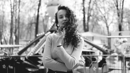 Obraz premium Girl chilling in amusement park in weekend morning. Laughing good-humoured female model with curly hair standing near carousel. Black and white photo