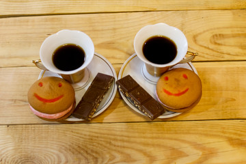Fragrant coffee with a cake in the form of a smile and chocolate in a plate on a wooden table