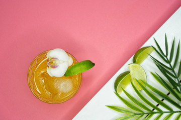 Tropical orange drink from above with limes and palm fronds on the side - an orchid garnishes the...