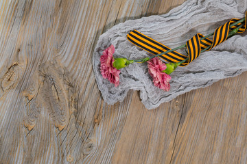 Two pink carnations, Saint George ribbon on a wooden surface.
