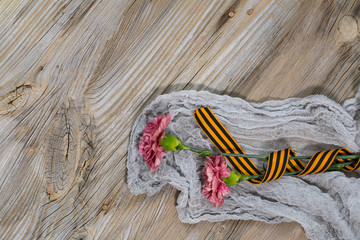 Two pink carnations, Saint George ribbon on a wooden surface.