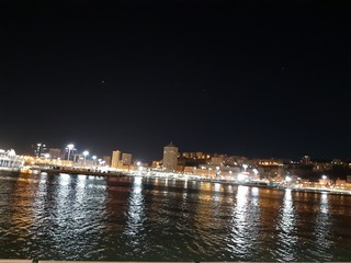 Fototapeta premium Genova, Italy - 04/19/2019: An amazing caption of the sea shore of Genoa by night in spring with some beautiful lights of the sheeps and a great view to a part of the city.
