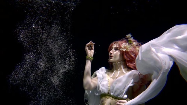 Woman model swimming in a dress like a mermaid underwater pool on a dark background like in a fairy tale