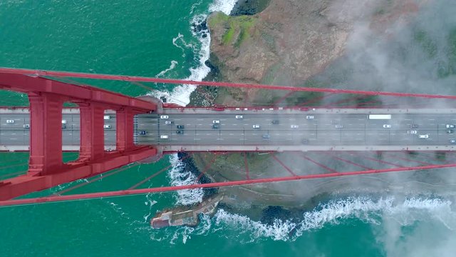 Aerial view of the Golden Gate Bridge. Cloudy fog soaring above the traffic on the red bridge over the green waters of the Pacific Ocean. San Francisco Bay, California, USA. Drone video