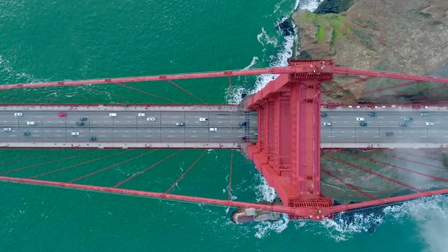 Aerial video of the Golden Gate. The busy road on the red bridge over the deep green Pacific Ocean. Fog drifting above the waves crashing the San Francisco Slow motion. California USA. Top view 4K