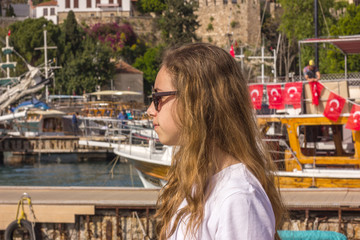 Young girl with long hair sits on the pier in the yacht port and looks at the blue sea